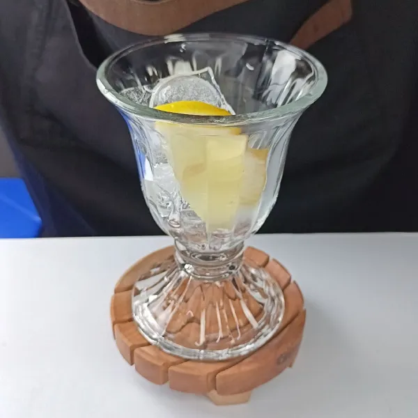 Tuang es batu dan lemon ke dalam gelas saji.