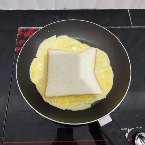 Lalu beri 1 lembar roti di atas telur. Lalu balik.