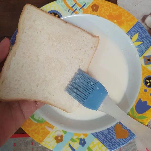 Ambil selembar roti tawar, olesi dengan susu cair.