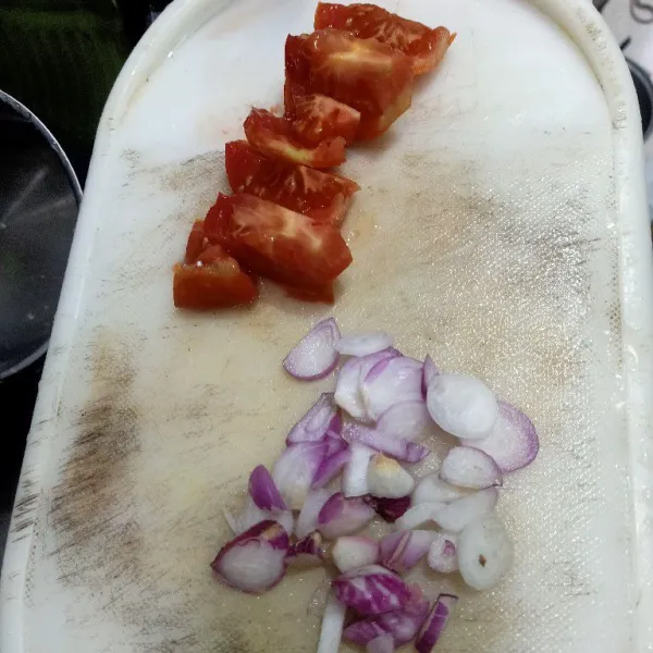 Kupas kulit bawang merah dan iris tomat. Sisihkan.