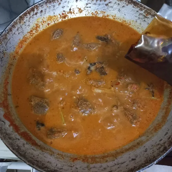 Tambahkan bumbu rendang instan ke dalam wajan, aduk rata, tambahkan air secara berkala sedikit demi sedikit hingga daging empuk, masak hingga bumbu kering.