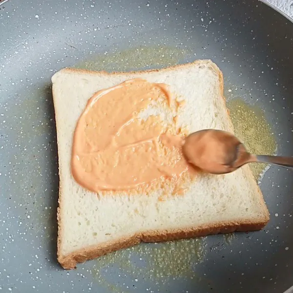 Ambil 1 lembar roti tawar lalu olesi dengan saos hingga rata.