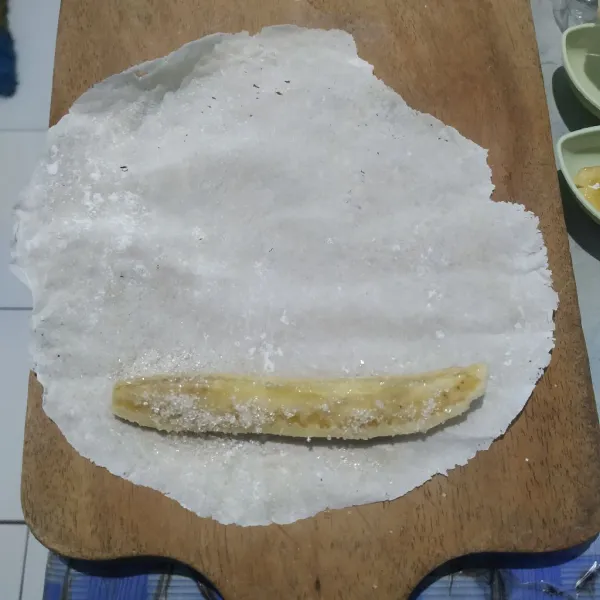 Letakkan pisang di ujung kulit lalu taburi dengan gula pasir kemudian gulung perlahan.