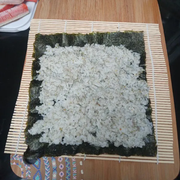 Siapkan tikar bambu, taruh nori di atasnya, tambahkan nasi, lalu ratakan.