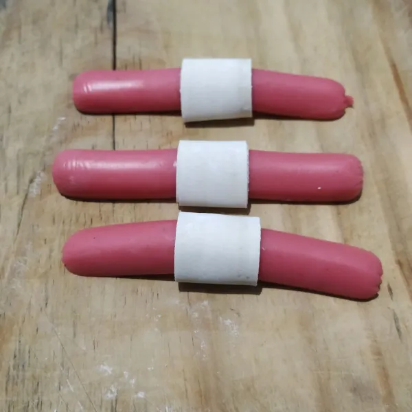 Lilitkan pangsit di bagian tengah sosis. Olesi ujung pangsit dengan air agar merekat.
