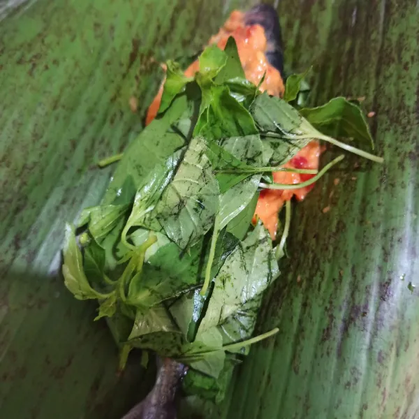 Ambil daun pisang, beri ikan, daun salam, daun kemangi dan tomat. Bungkus rapi.