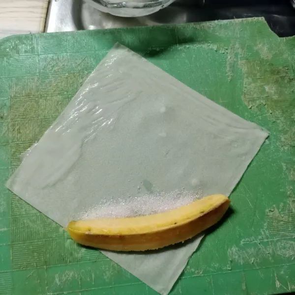 Ambil 1 lembar kulit lumpia, letakkan 1 potong pisang dan 1 sdt gula pasir diatasnya. Olesi pinggiran kulit lumpia dengan larutan terigu.