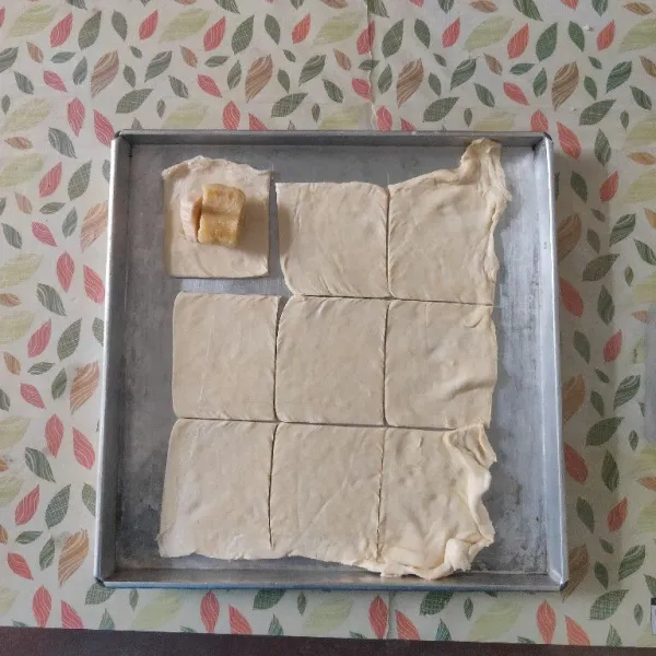 Siapkan loyang, lalu letakkan satu lembar kulit puff pastry, potong menjadi 9 bagian. Tambahkan pisang dan keju.