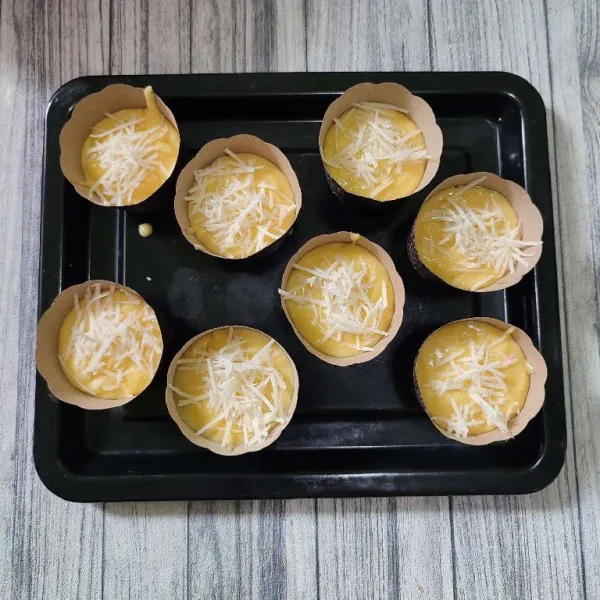 Masukkan adonan ke dalam cup muffin, isi ¾ bagian saja. Lalu beri taburan keju parut.