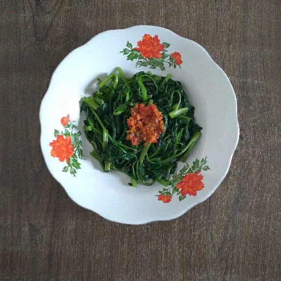 Tata sayur kangkung di piring lalu tambahkan sambal bawang di atasnya.