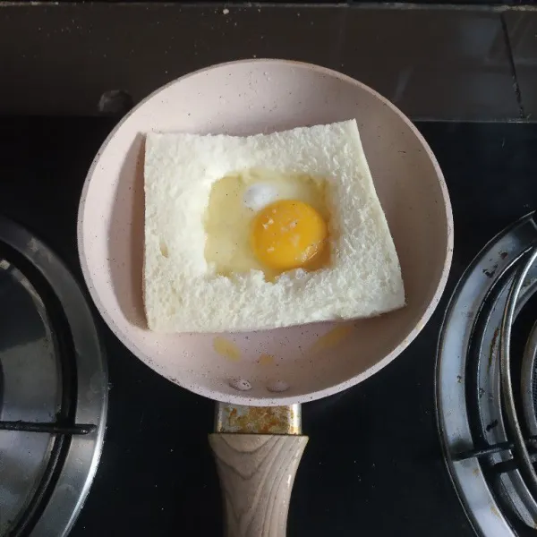 Pecahkan telur ke tengah roti, beri garam dan merica. Biarkan matang.