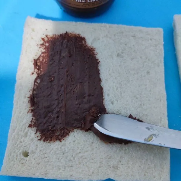 Siapkan roti tawar, oles salah satu sisi dengan selai cokelat kacang.