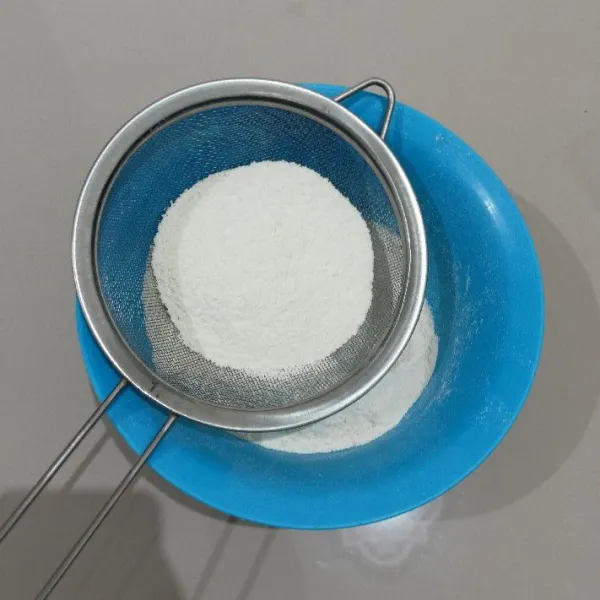 Ayak tepung terigu, baking powder, baking soda dan garam di dalam mangkuk.