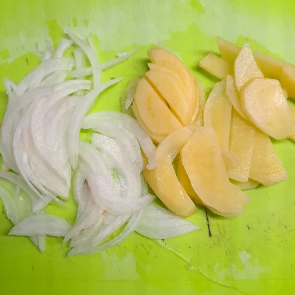 Kupas dan iris tipis kentang. Iris kasar bawang bombay.
