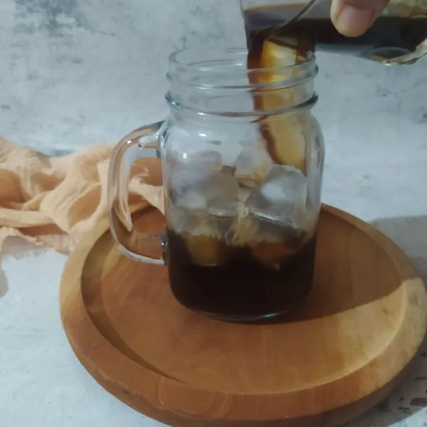 Tuang larutan kopi ke dalam gelas berisi es batu.