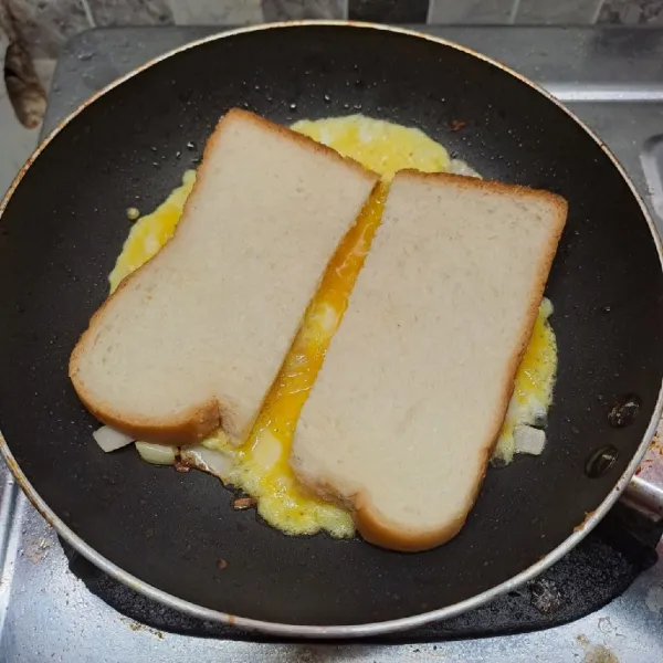 Belah dua roti tawar, letakkan di atas telur yang masih basah. Beri jarak, agar nanti dapat dilipat.