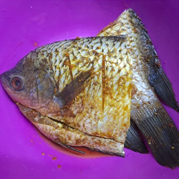 Haluskan bawang putih, kunyit, ketumbar, dan garam. Balur rata di tubuh ikan yang sudah dikerat. Marinasi minimal 15 menit agar meresap.