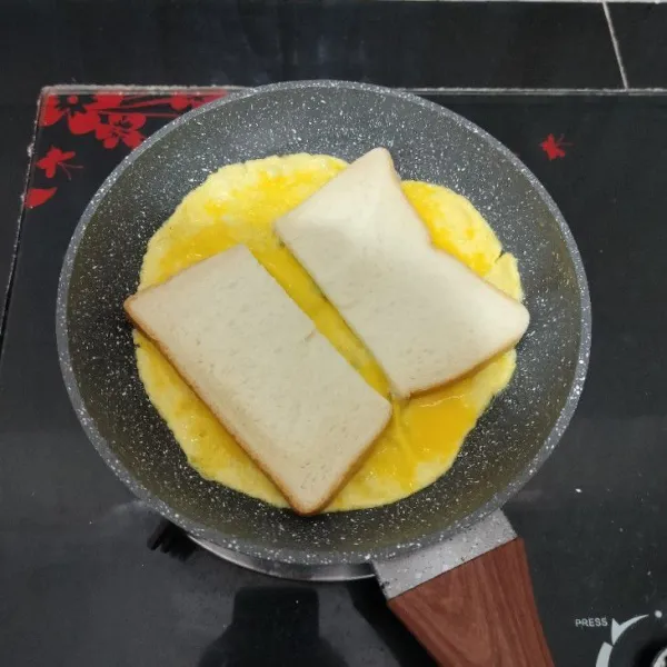 Ketika bagian atas telur masih basah, letakkan roti tawar di atasnya. Masak hingga bagian bawah telur matang.