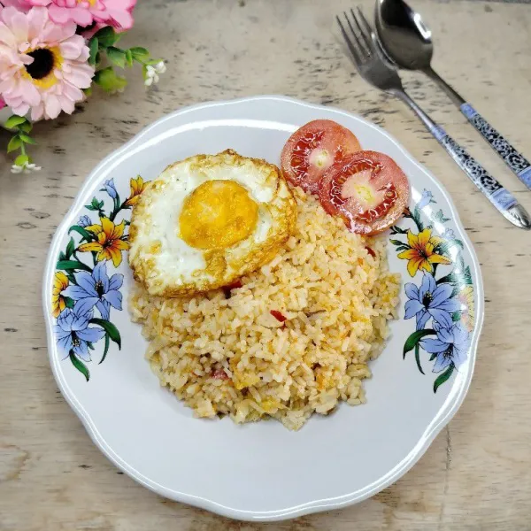 Tata nasi goreng di piring. Sajikan dengan telur ceplok dan irisan tomat.