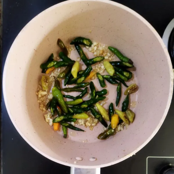 Tumis irisan bawang merah dan bawang putih hingga harum, lalu masukkan irisan cabai hijau dan cabai rawit hijau, tumis lagi selama 3 menit.