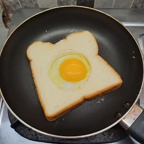 Panaskan teflon dengan api kecil saja. Lelehkan margarin, panggang roti, kemudian beri telur di dalam lubang roti.
