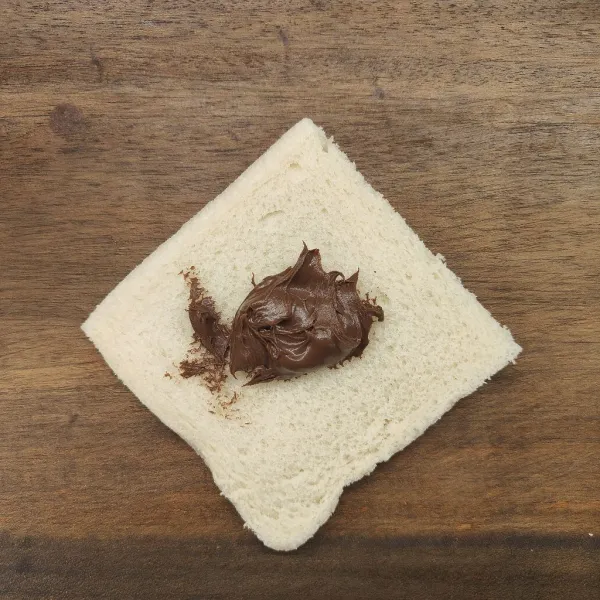 Ambil 1 lembar roti tawar, taruh selai coklat di tengahnya.