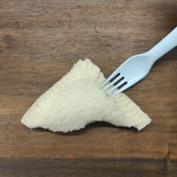 Lipat roti bentuk segitiga, lalu tekan dengan garpu bagian pinggirnya.
