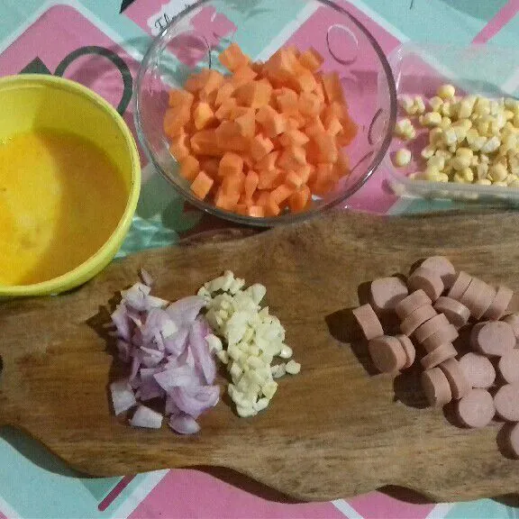 Siapkan bahan nasi goreng. Potong kotak kecil wortel dan iris tipis sosis. Cincang halus bawang putih dan merah.