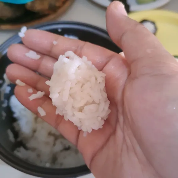 Celupkan tangan ke campuran air, ambil nasi dan kepalkan perlahan supaya mendapatkan bentuk gumpalan nasi yang masih utuh, celupkan kembali tangan ke dalam air untuk mengepalkan nasi, lakukan berulang.