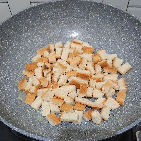 Tata pinggiran roti tawar yang sudah dipotong dadu ke dalam teflon.