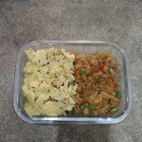 Tata nasi di dalam wadah, tambahkan scrambled egg, beri topping sosis, tomat merah dan sayur, kemudian sajikan.