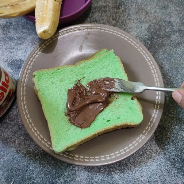 Oleskan permukaan roti tawar dengan selai cokelat.