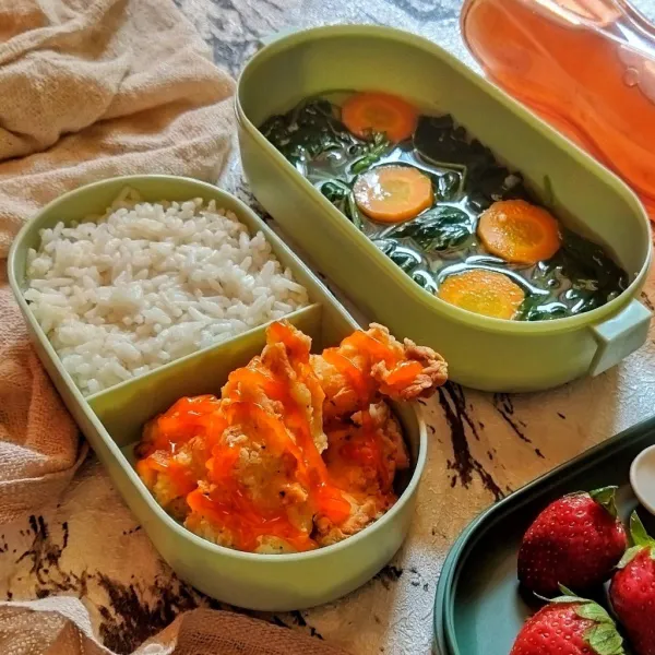 Tata pada wadah bekal, ayam goreng, topping dengan saus sambal, tambahkan nasi putih, sayur bening bayam, dan buah strawberry. Sajikan sebagai bekal.