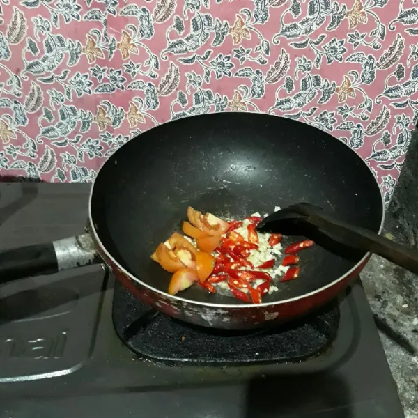 Tumis bawang putih hingga harum, lalu masukkan cabai dan tomat. Aduk rata.