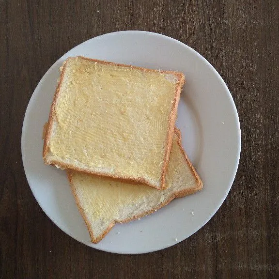 Olesi roti tawar dengan mentega di satu sisi.