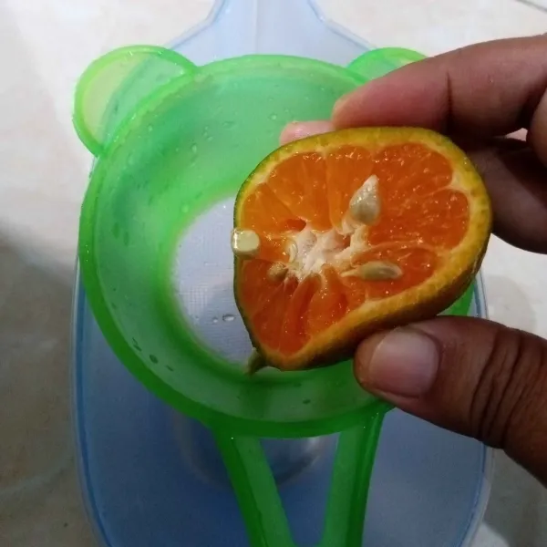 Belah jeruk menjadi dua bagian lalu peras airnya.