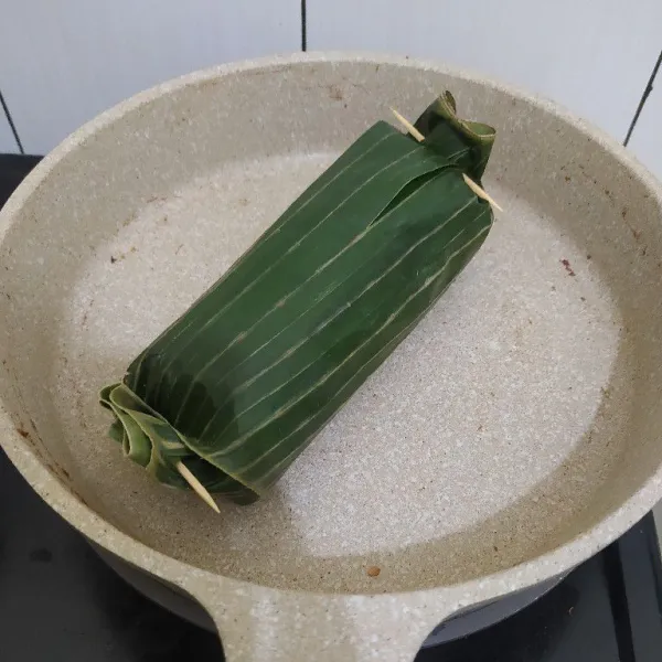 Tata 2 centong nasi di atas daun pisang, lalu beri atasnya dengan ikan tongkol suwir. Gulung daun pisang dan sematkan dengan lidi. Lalu bakar diatas teflon hingga permukaannya layu. Tata di wadah bekal. Sajikan.