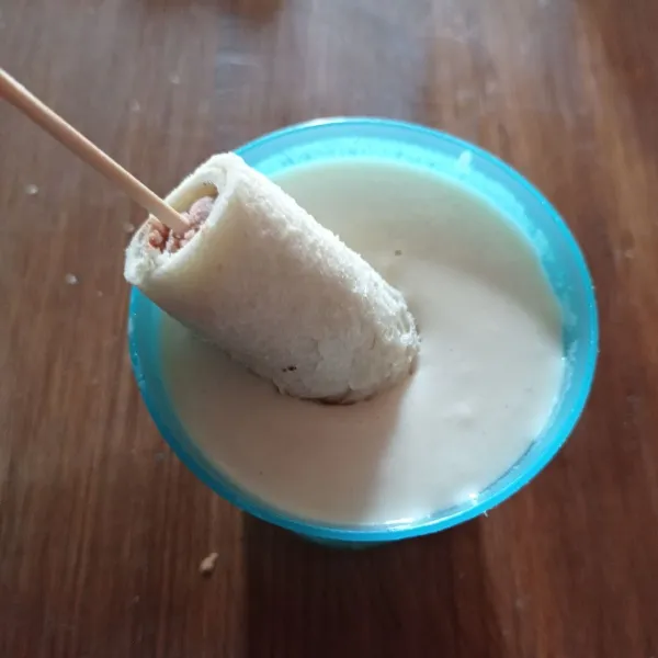 Ambil 1 bagian corn dog beri tusuk sate lalu celupkan ke adonan tepung.