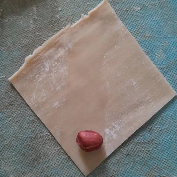 Ambil selembar kulit pangsit kasih air di tengahnya taruh kacang di pinggir.