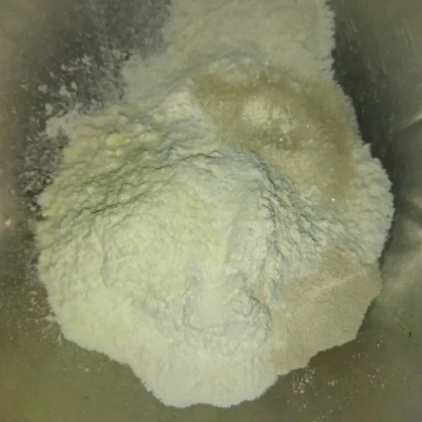 Siapkan wadah, masukkan tepung terigu, susu bubuk, gula pasir, dan ragi instan, aduk rata, lalu masukkan campuran telur dan air es, aduk rata hingga adonan menggumpal.
