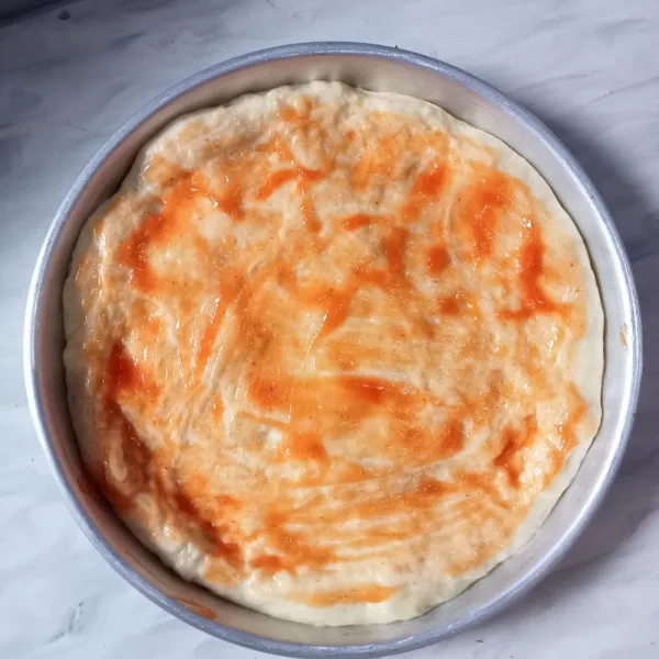 Ambil satu bagian, tata di loyang pizza. Diamkan selama 30 menit (atau sampai mengembang), lalu tusuk-tusuk adonan pizza dengan garpu dan olesi dengan saus.