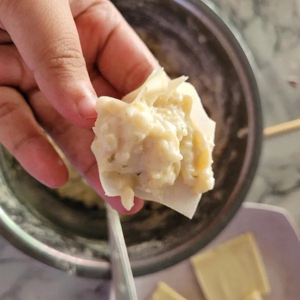 Potong kulit pangsit menjadi bentuk persegi, adonan yang telah tercampur diletakkan diatas kulit pangsit dan dibentuk bulat menyerupai dimsum.