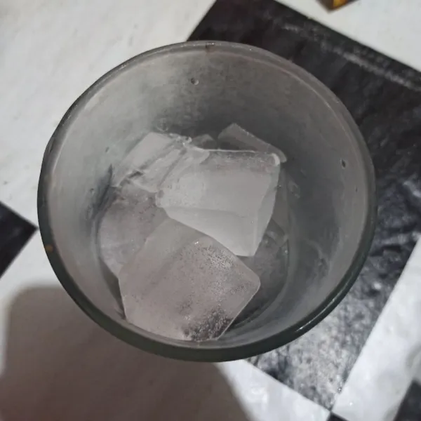 Tuang es batu ke dalam gelas saji.