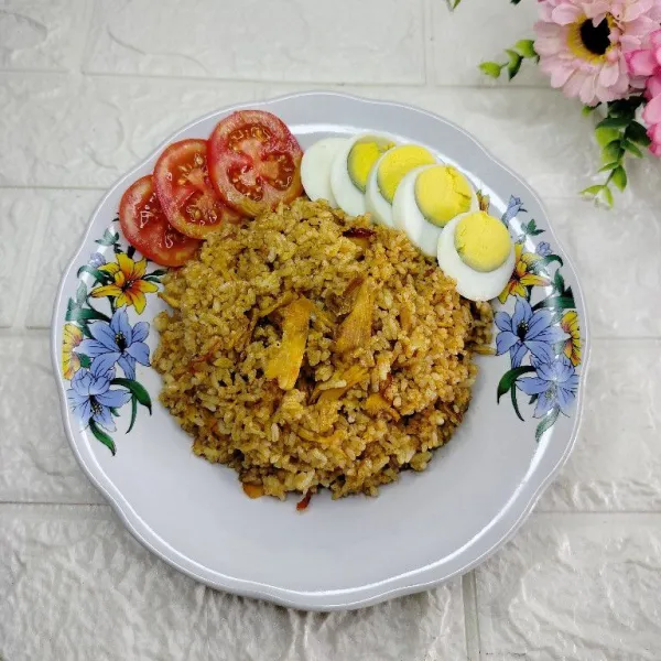 Tuang nasi goreng di piring. Sajikan dengan irisan telur rebus dan tomat merah.