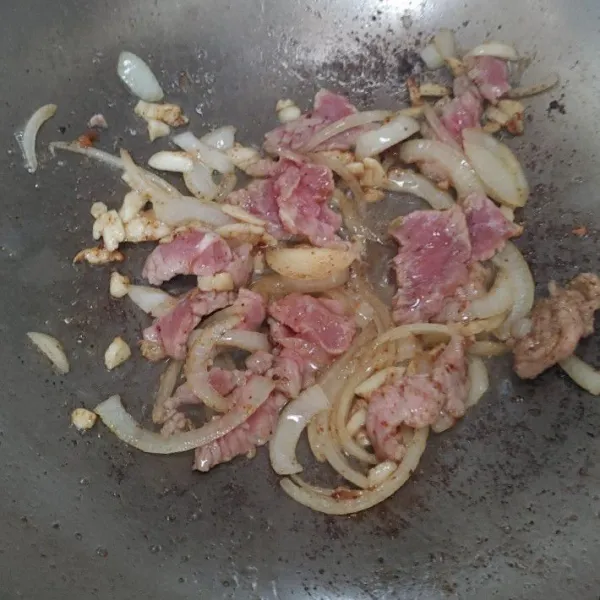 Tumis bawang putih dan bawang bombay hingga harum, lalu masukkan irisan daging sapi, aduk rata.