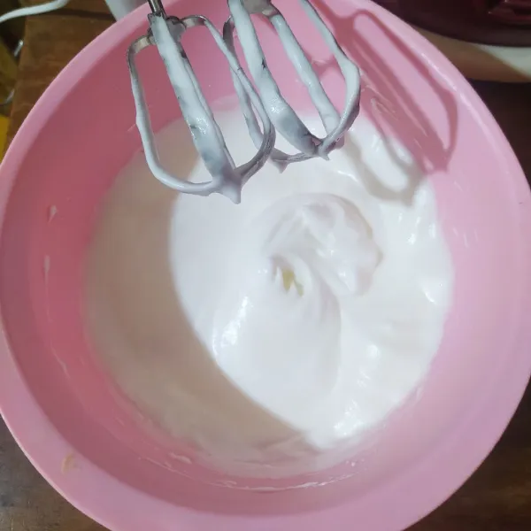 Dalam wadah lain, masukkan putih telur lalu mikser. Masukkan gula secara bertahap sambil terus di mikser sampai soft peak (ketika mixer diangkat dari kocokan putih telur, puncak adonan akan mengecil dan melengkung ke bawah).