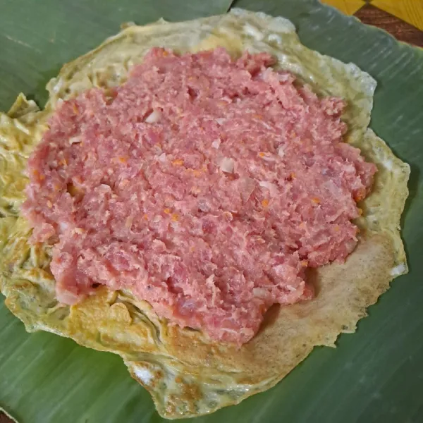 Ambil selembar dadar telur. Beri ½ adonan daging secara merata.