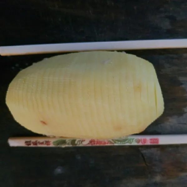 Letakan sumpit dikedua sisi kentang, lalu iris tipis-tipis kentang.