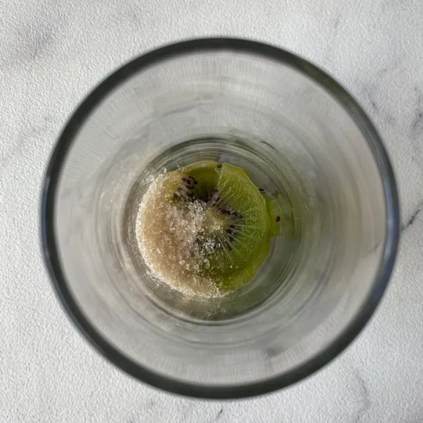 Kupas kiwi, cuci bersih lalu potong-potong dan masukkan ke dalam gelas dengan gula pasir. Lumatkan menggunakan sendok sampai kiwi hancur.