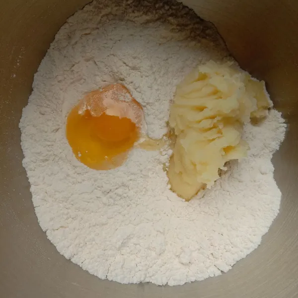 Dalam sebuah wadah, masukkan tepung terigu, gula pasir, dan santan bubuk, lalu aduk rata. Masukkan kentang kukus halus dan telur